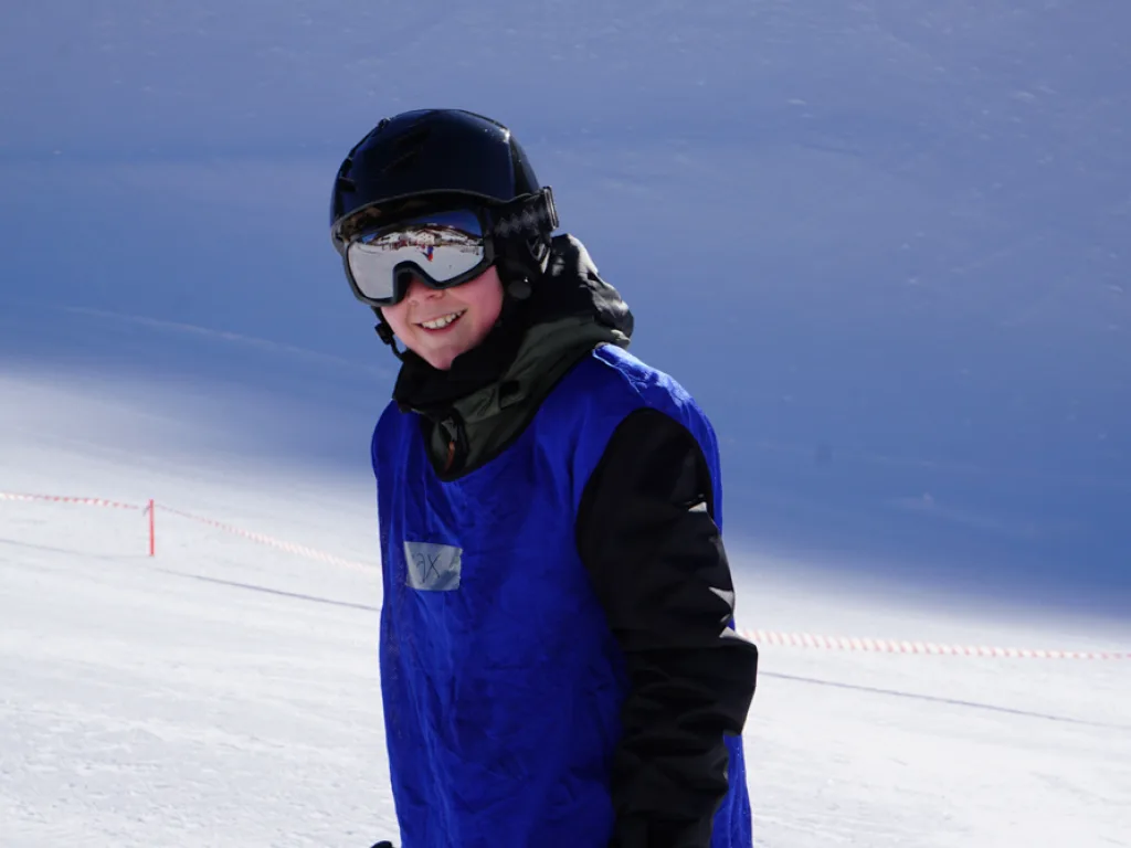 Jugendlicher lacht auf der Piste in die Kamera.